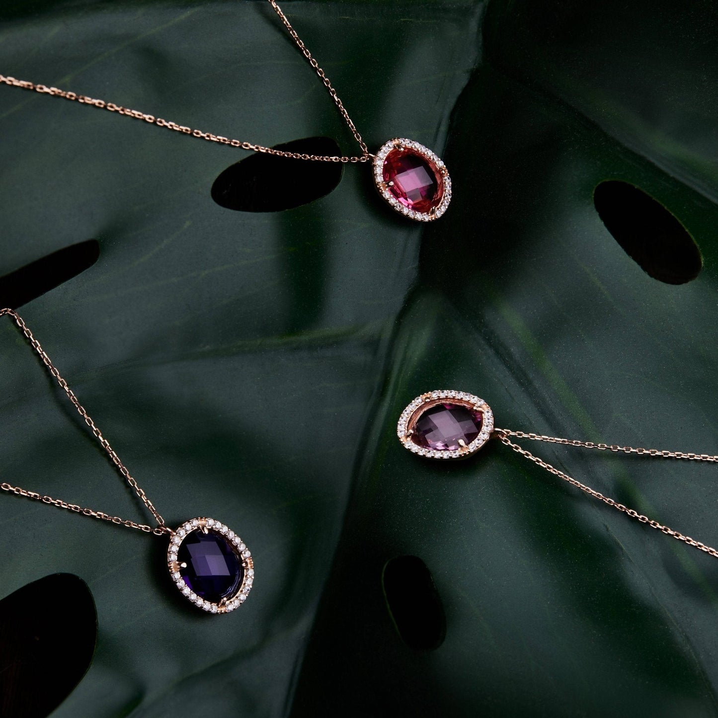 Two necklaces with gemstone pendants on a dark green leaf.